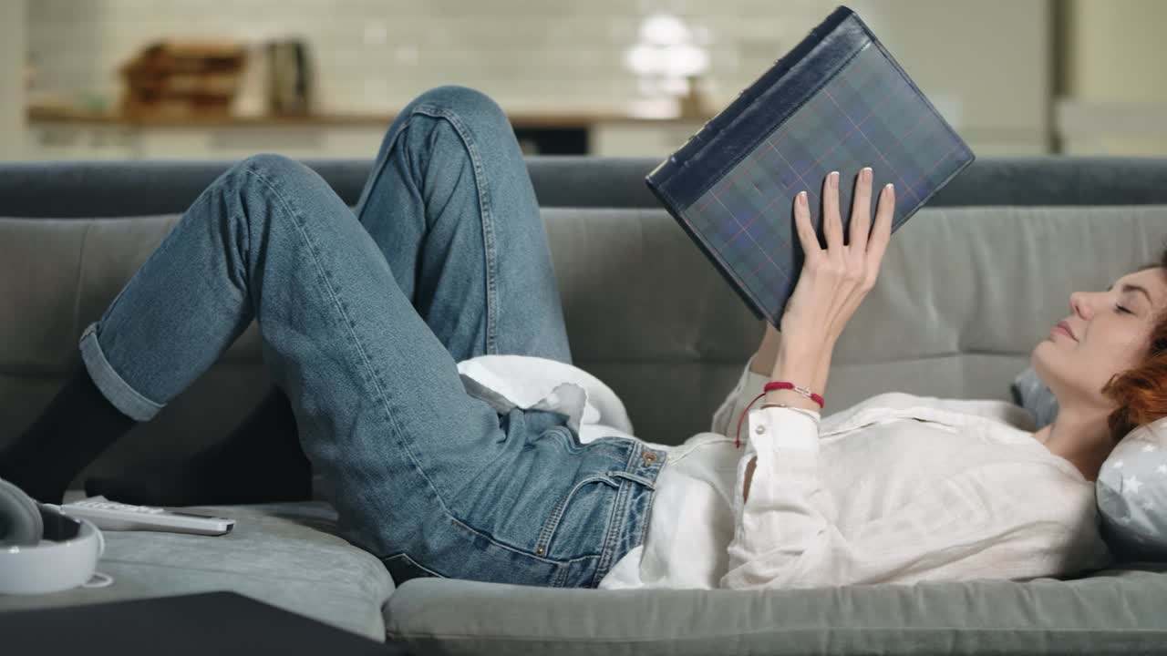 소파에 사진책을 찾는 아름다운 여자. 사진 앨범을 벗는 편안한 소녀