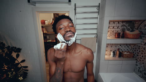 young black man applying shaving cream to face in bathroom