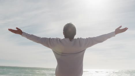 Back-view-of-hispanic-senior-woman-standing-on-beach-and-raising-hands