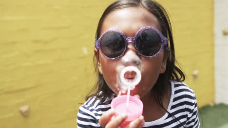 in a schoolyard, a young biracial girl is blowing bubbles