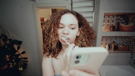 gen z girl brushing teeth and checking her phone in bathroom