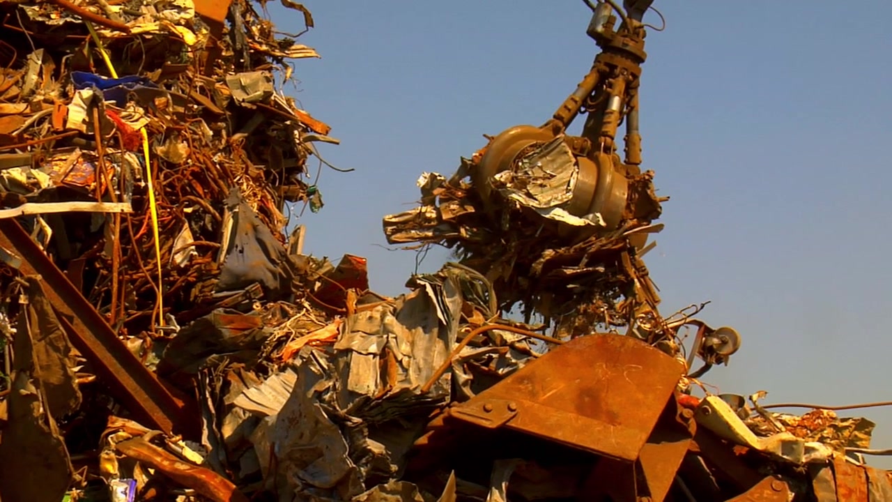 A hydraulic claw lifts rusty metal scrap in an industrial yard, emphasizing recycling, sustainability, and heavy machinery at work.