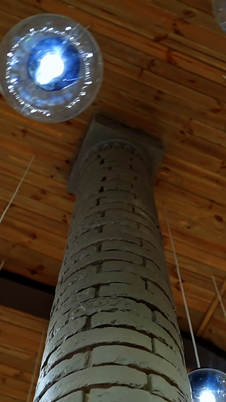 Modern ceiling with light lamp balls. Many round light balls hanging around brick column in the hall. Beautiful glass bulbs on brown background. Vertical video