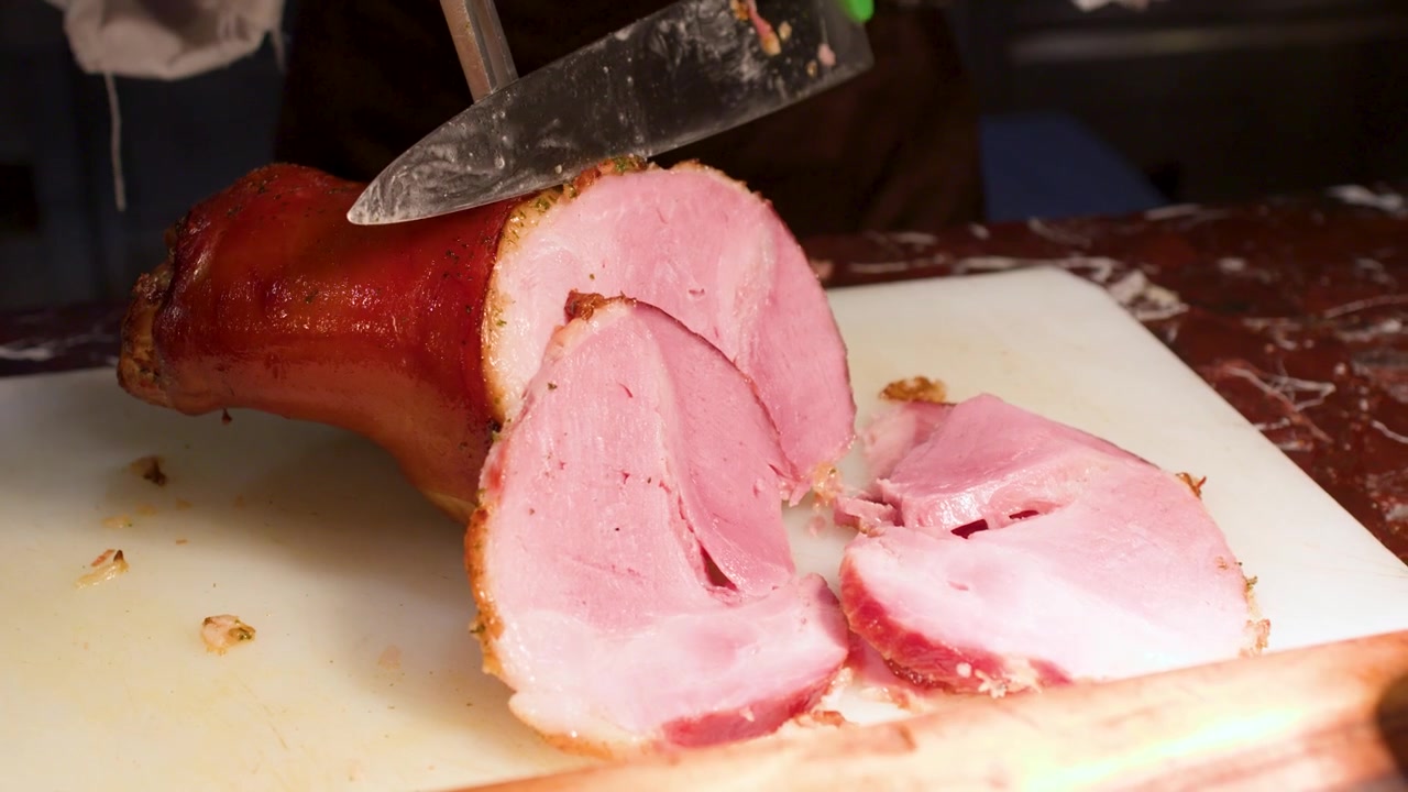 Primo piano di uno chef che taglia fette sottili di prosciutto arrosto a una stazione buffet