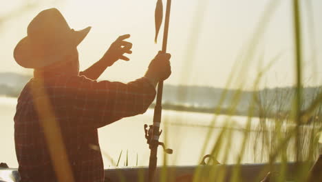 side view of a senior caucasian man in a hat catching a fish in a boat at the lake in the morning