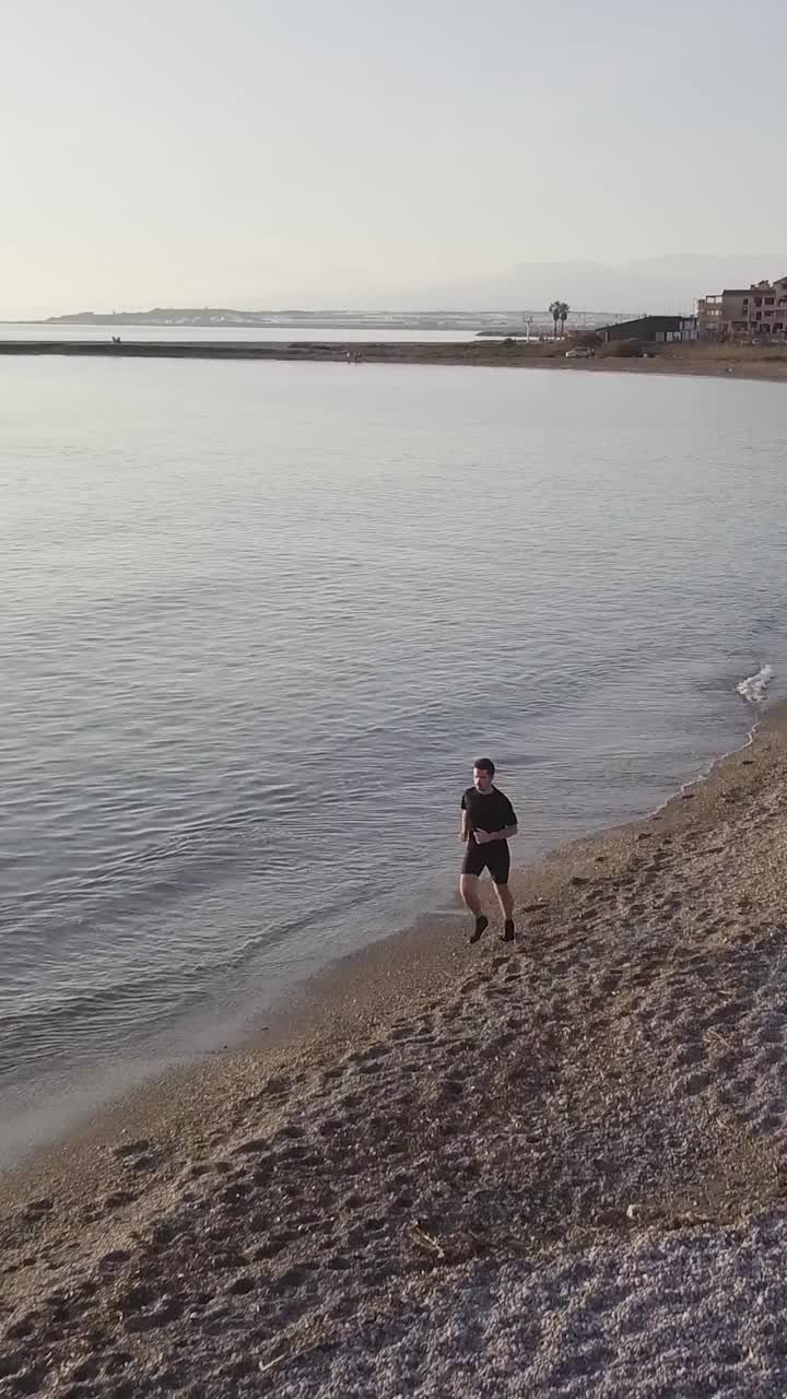 Young runner man training on beautiful sunset at beach. Drone view