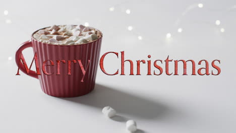 texto de feliz navidad en rojo sobre chocolate caliente con malvaviscos en fondo gris