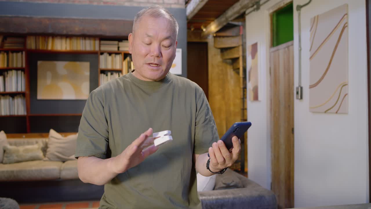 カウンターで、アジア系の高齢男性が青いスマートフォンで設定を行い、白いデバイスを裏返して画面を見せている。