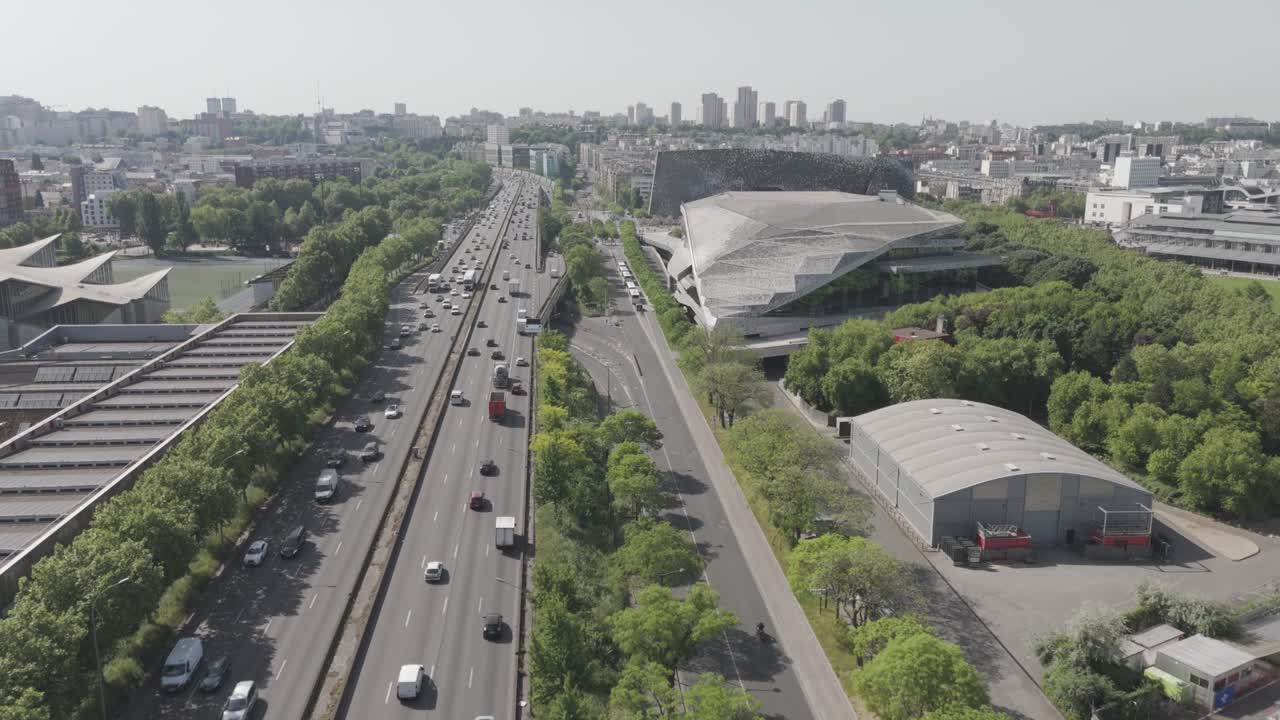 Drone footage advancing over the Paris ring road (périphérique), showcasing buildings, greenery, and distant skyscrapers in the Paris suburbs - France