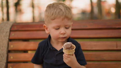 un niño lindo come helado en un cono de obleas en un banco