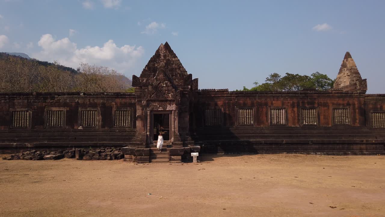 una joven hermosa viajera con un largo vestido blanco y gafas de sol sale del palacio khmer en wat phou, un complejo de templos hindú en ruinas. champassak, laos, asia. cultura antigua arquitectura religiosa.