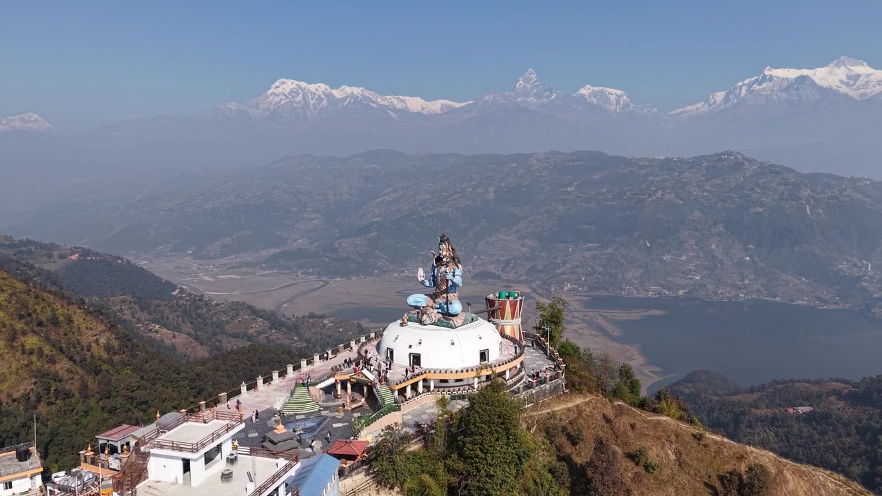 Imagem de drone em grande angular do icônico monumento de Shiva em um cume de colina com picos nevados distantes do Himalaia