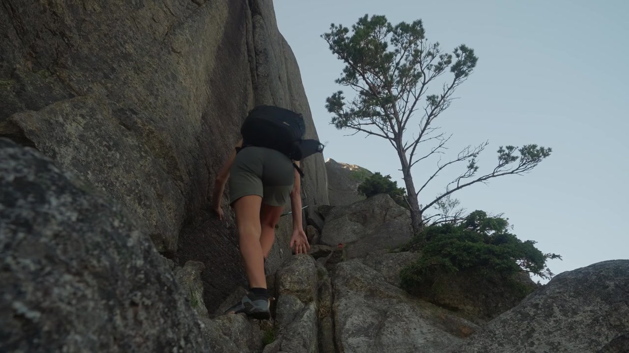 Mulher ativa e em forma caminha e escala enormes rochas verticais de granito ao ar livre, demonstrando equilíbrio, mobilidade e grandes movimentos de pisada em terreno natural acidentado na Noruega.