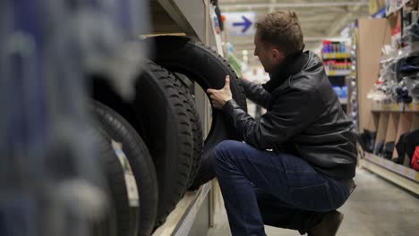 Young-man-in-supermarket-choosing-automobile-tyres-standing-on-the-shelves