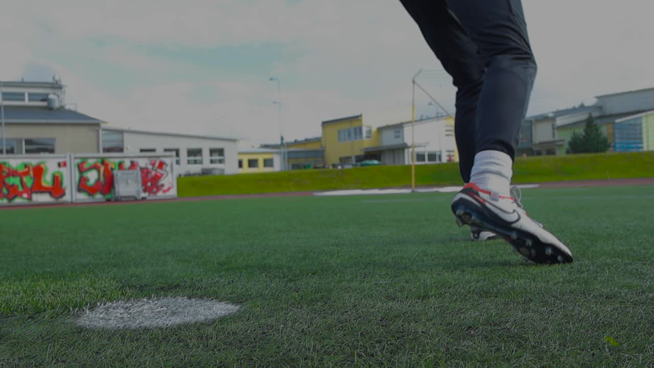 Close up footage of a soccer ball being kicked and hit on a soccer stadium during summer time while its cloudy in slow motion. Ball is placed on white penalty marking on the short stadium grass.