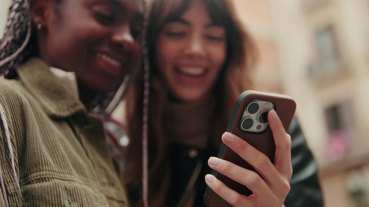 Two Happy Young Women Laughing While Using Smartphone Outdoors