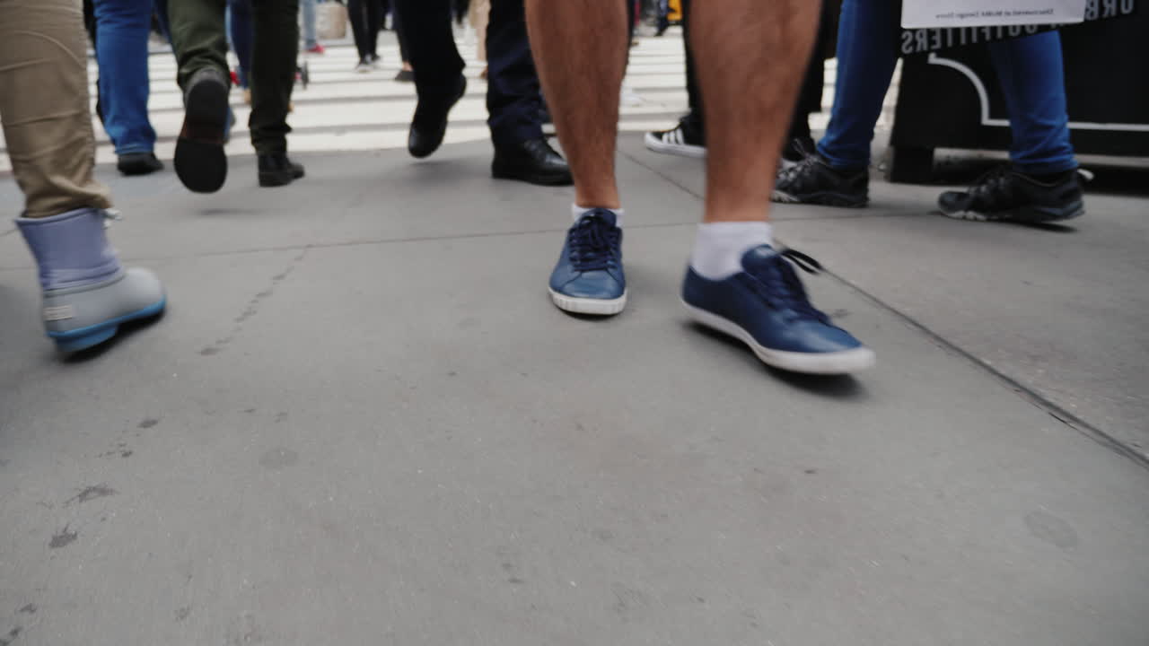 una mujer con una bolsa de viaje sobre ruedas va a un paso de peatones en una multitud de personas que solo tienen piernas