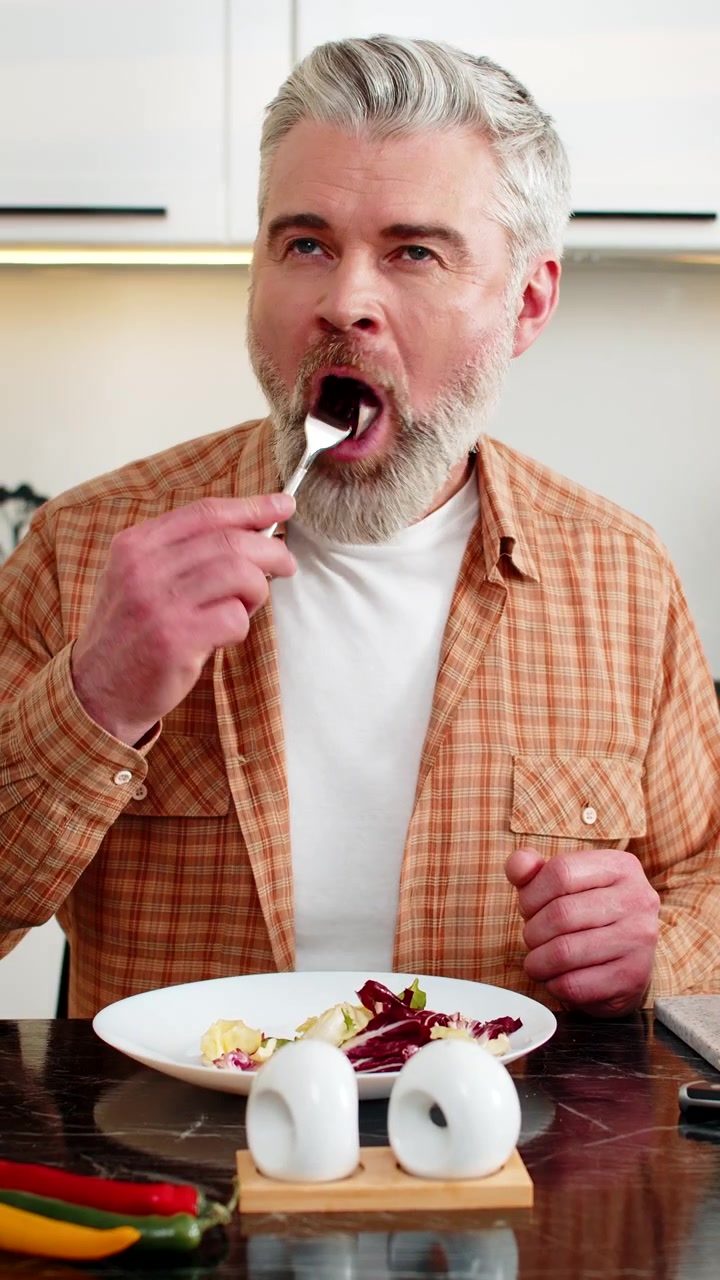 Uomo di mezza età che gusta un'insalata di verdure fresche nella cucina di casa per uno stile di vita basato su una dieta sana e nutriente.
