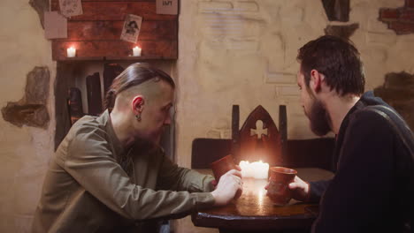 man listens to friend sitting in tavern.bearded adventurers share secret information looking aside in medieval pub. historical inn guests communicate