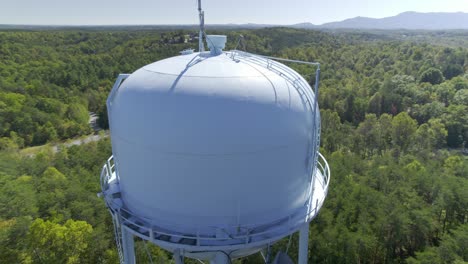 Approaching-a-water-tower-peaking-through-a-dense-forest-as-a-hawk-flies-from-the-top