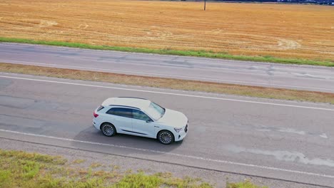 View from above on luxury white car on the highway. Beautiful audi driving along the road among yellow fields. Aerial view.