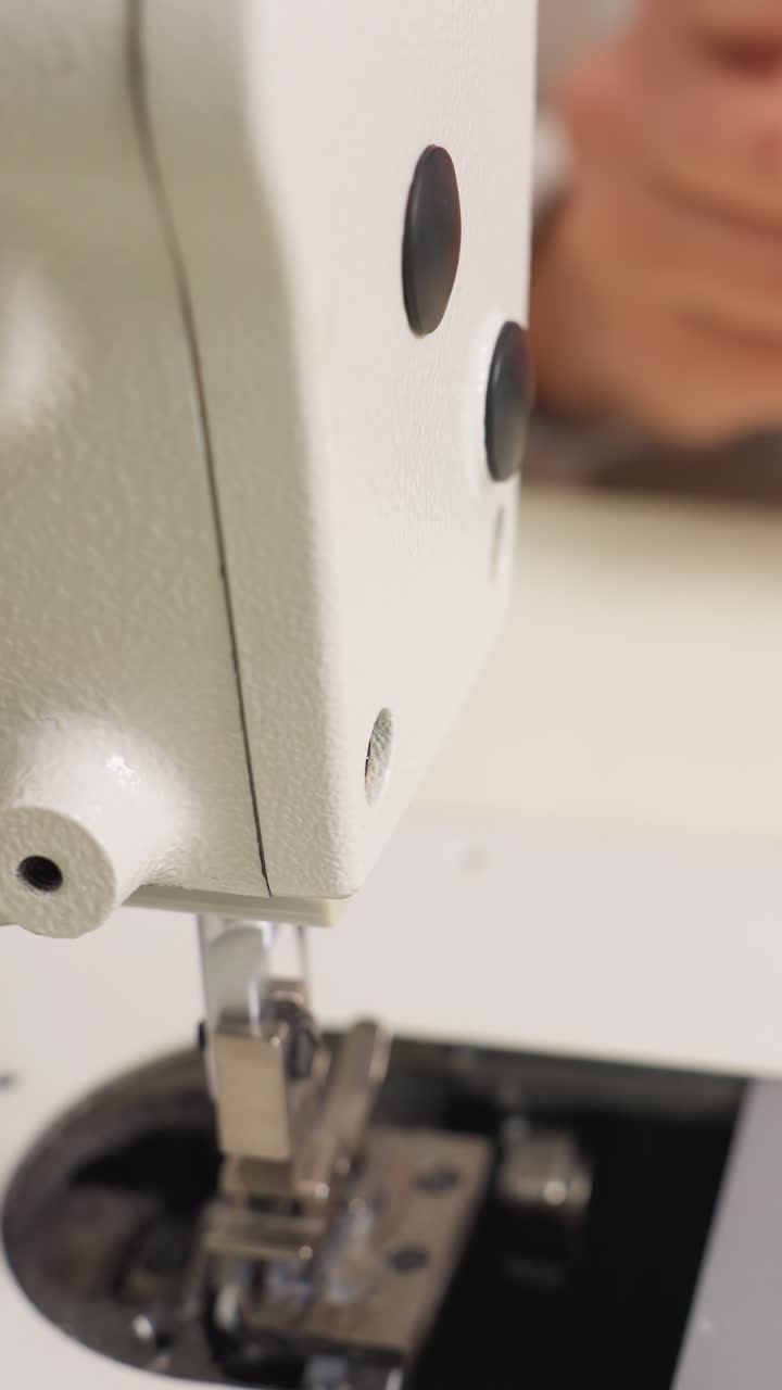 Primer plano de manos caucásicas sobre el prensatelas, placa metálica y garganta de la aguja visibles, ajuste delicado de la tensión y el hilo, vista macro del mecanismo de alimentación y acción de costura, técnica enfocada