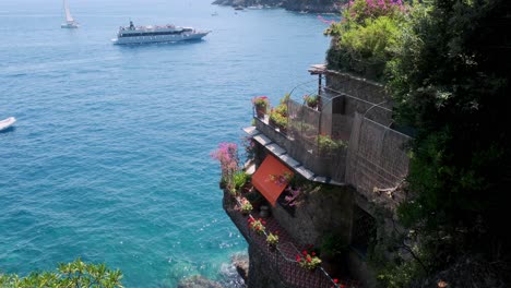 view of the mediterranean sea from a cliffside balcony adorned with vibrant flowers in portofino,a large tourist boat cruises along the crystal blue waters, with a sailboat in the distance