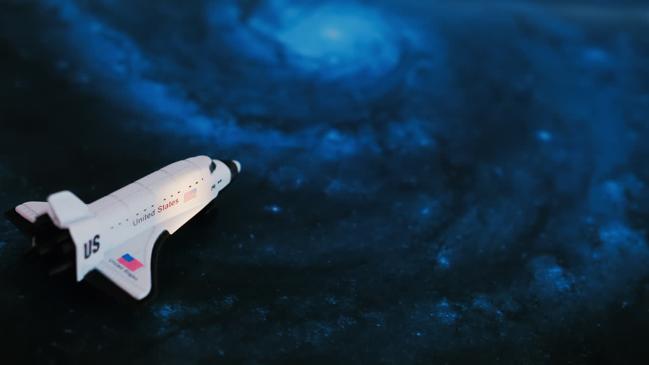 Close up of a miniature toy space shuttle placed on a blue cosmic galaxy backdrop