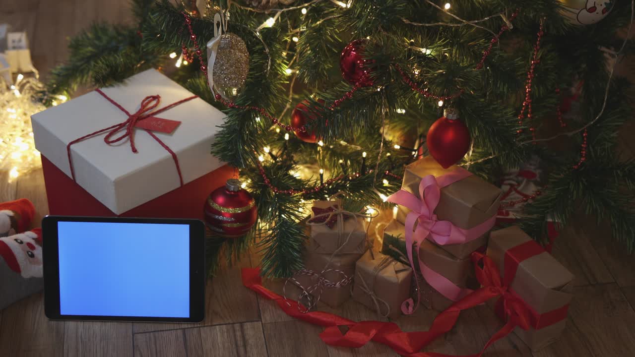 navidad cajas de regalos de artesanía rojas y tableta pantalla de maqueta azul bajo el abeto