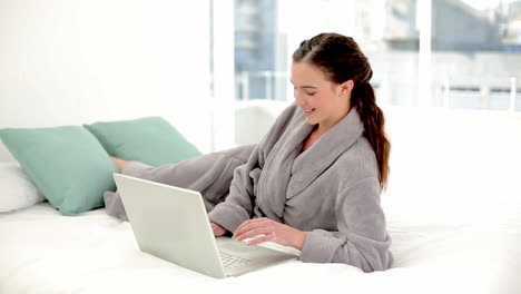 Peaceful-brunette-woman-using-her-notebook-wearing-a-bathrobe-