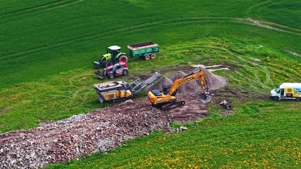 Construction site in green field with excavator, tractors, and rubble piles