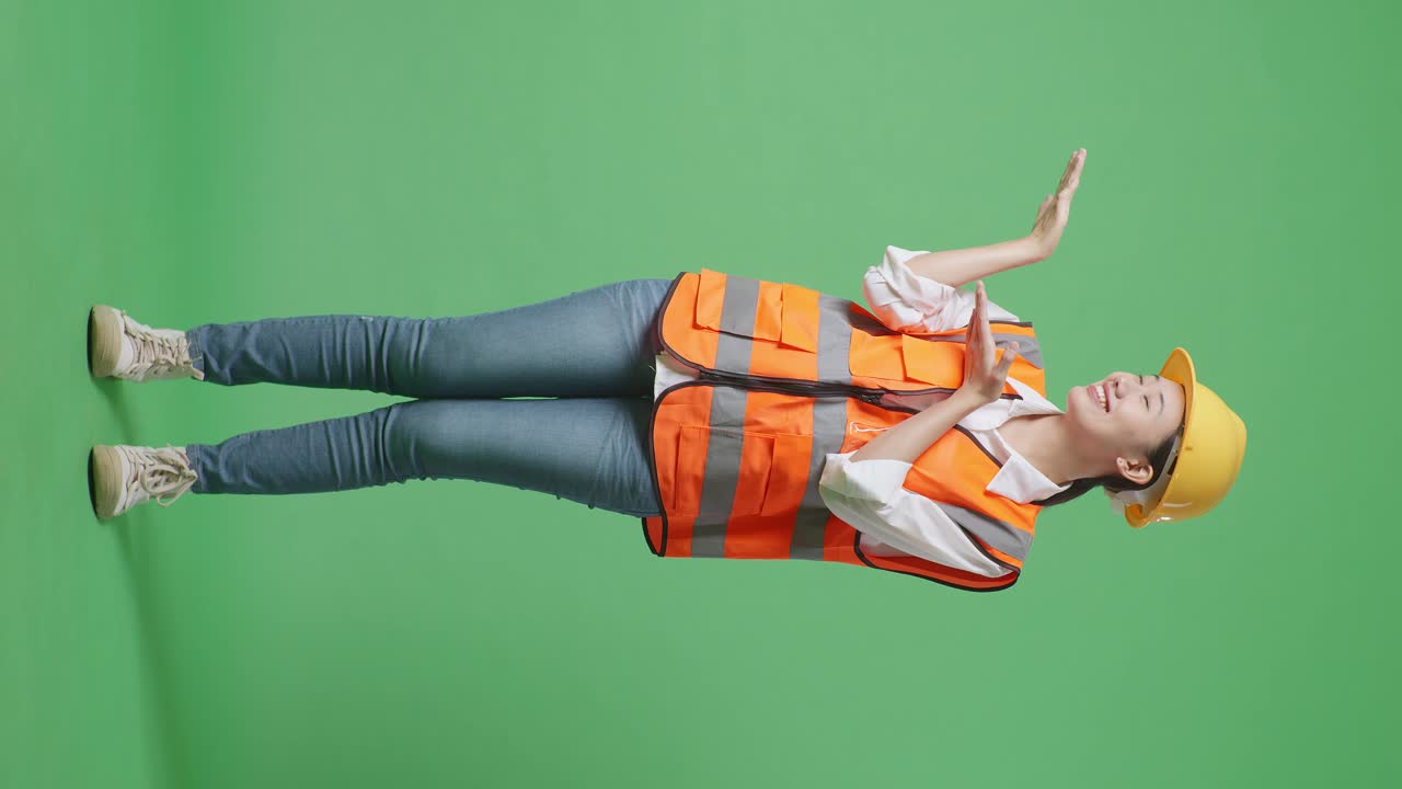 Full Body Of Asian Female Engineer With Safety Helmet Smiling And Pointing To Side While Standing In The Green Screen Background Studio