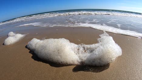 Lowering-down-towards-slow-motion-close-up-of-sea-foam-as-it-billows-from-the-breeze