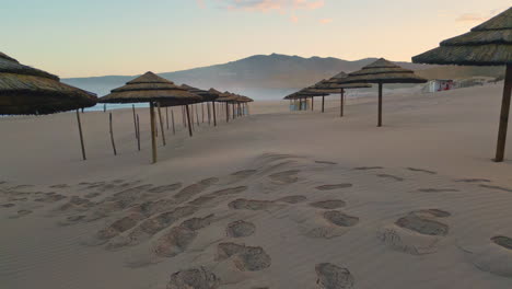 avión no tripulado volando rápido sombrillas de paja playa de primer plano. puesta de sol paisaje de balneario de arena