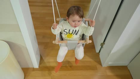 adorable caucasian two years old baby sitting in a doorway swing - top angle view