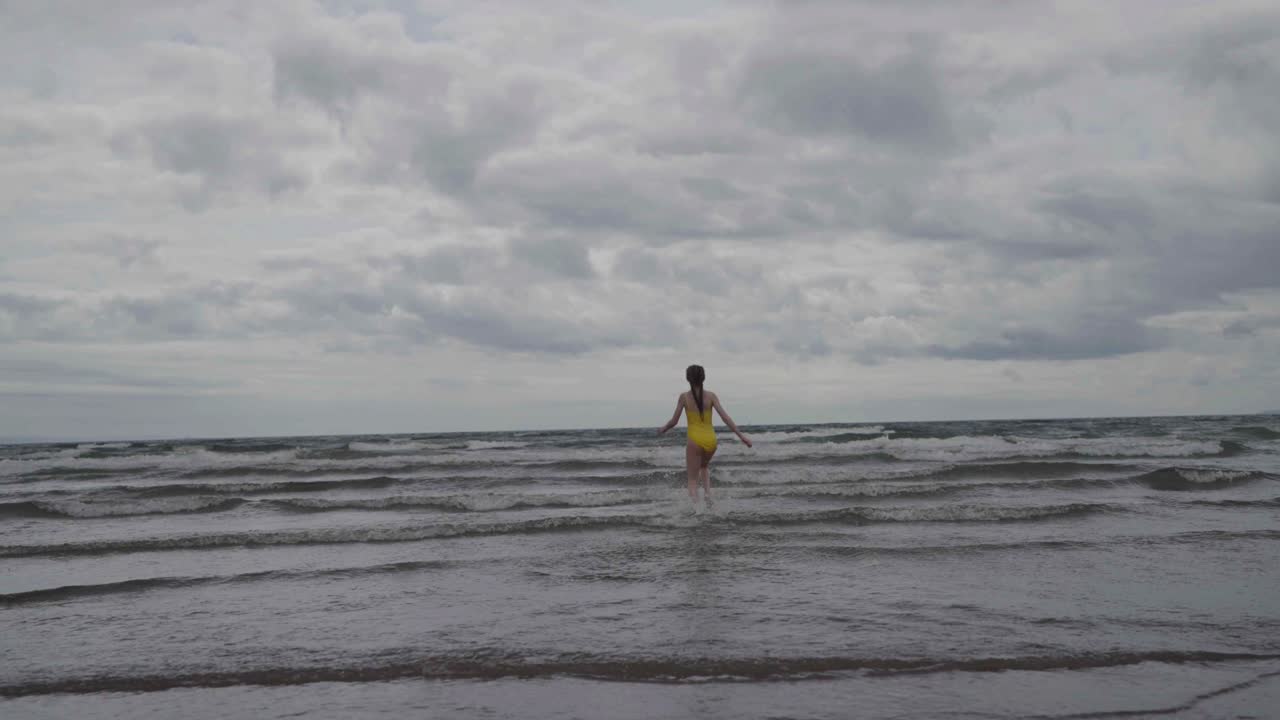 노란색 수영복을 입은 어린 소녀가 바다로 뛰어들고, 느린 움직임