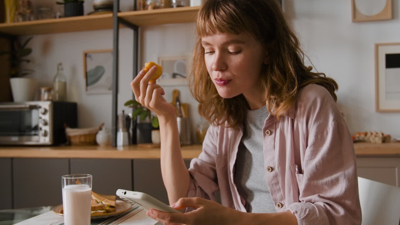 Woman eating breakfast while using smartphone in kitchen
