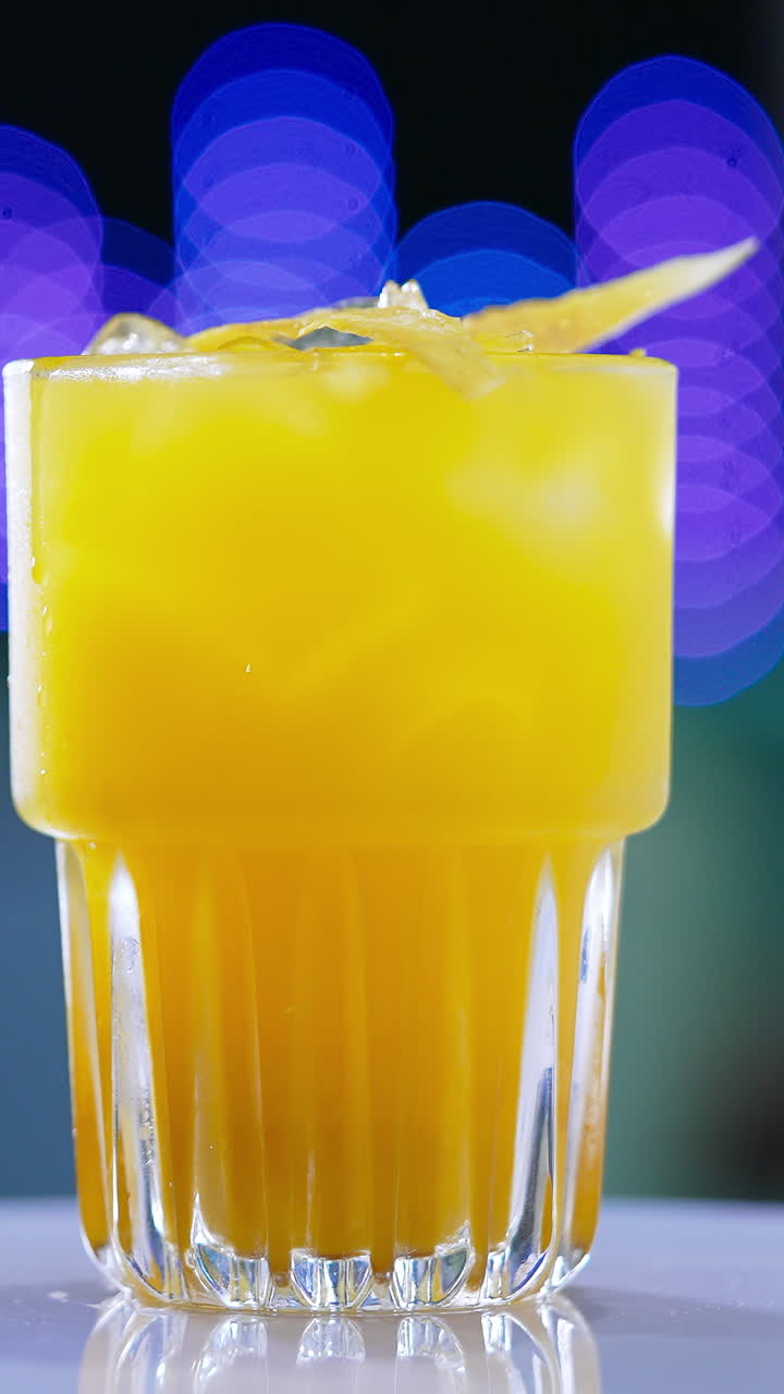 A glass filled to the top with beverage of yellow color. Savory cocktail on the rotating table close up. Blurred backdrop. Vertical video