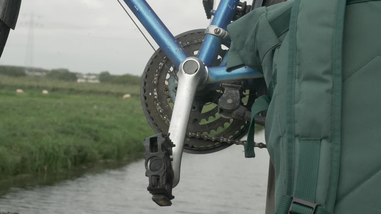 primer plano de un pedal de bicicleta vacío y una mochila con un arroyo al fondo