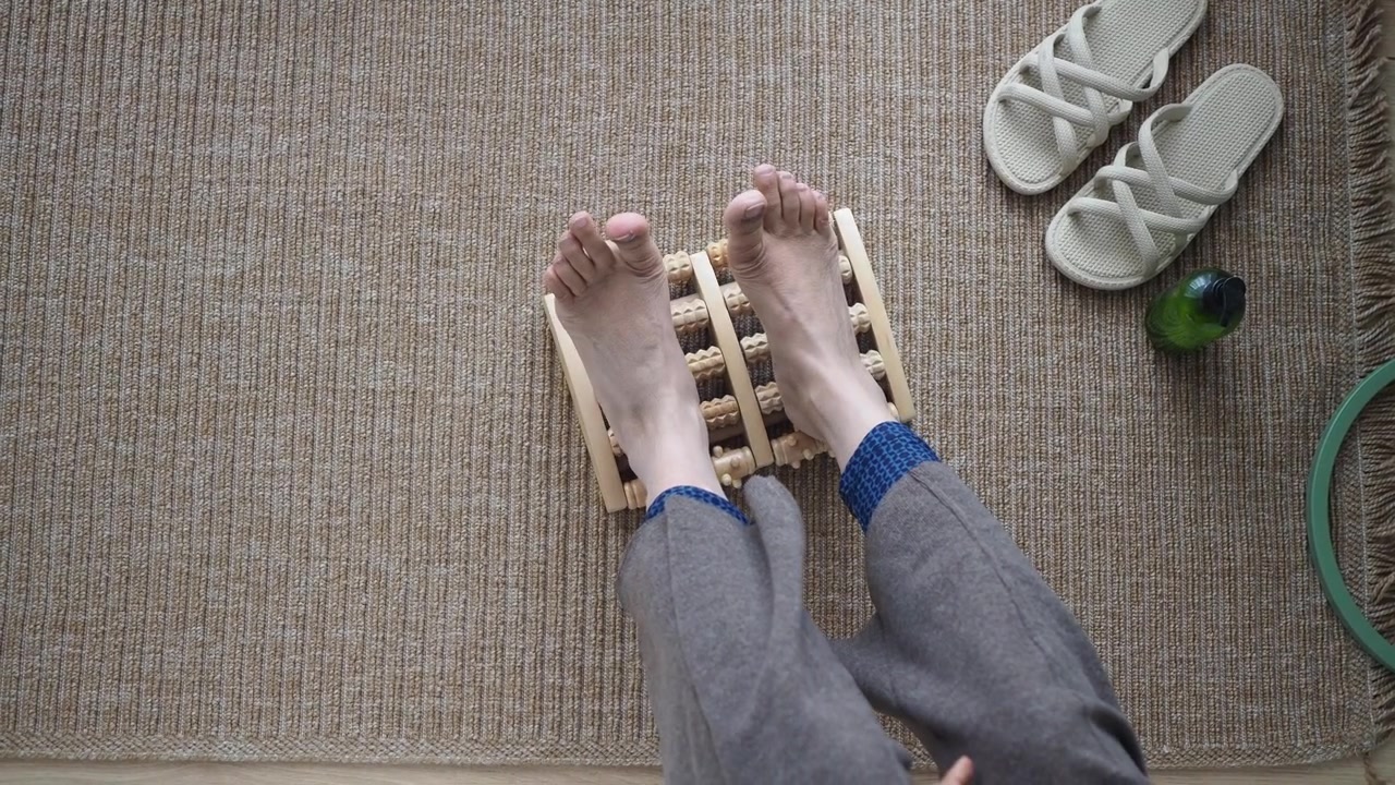 Persona che utilizza un massaggiatore a rullo in legno per piedi su un tappeto.