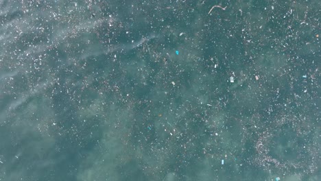 Top-down-descending-drone-shot-of-polluted-water-filled-with-plastic-trash-and-dead-coral-reef-in-the-turqouise-tropical-water-of-Bali-Indonesia