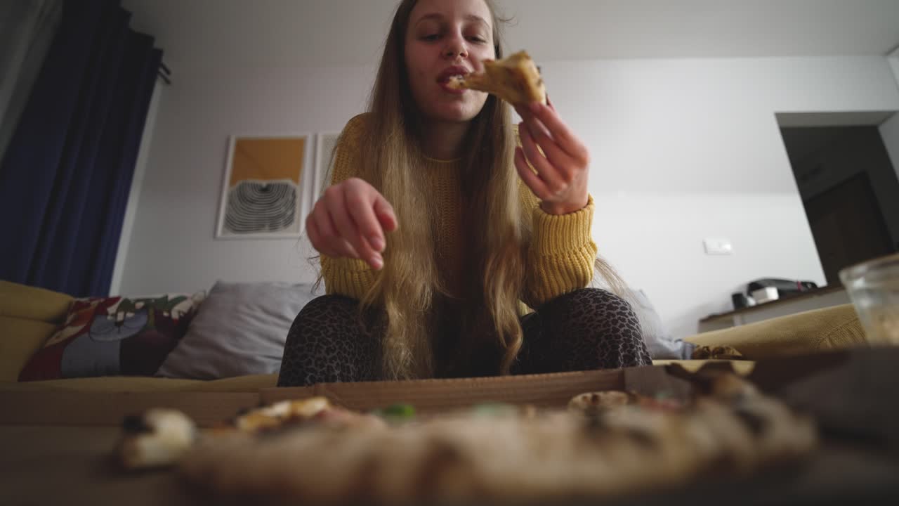 Donna che addenta una fetta di pizza da un ordine di fast food, mostrando piacere, soddisfazione e golosità mentre mangia, catturando lo stile di vita del fast food e l'esperienza di ristorazione informale.
