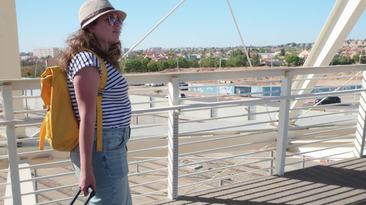 A woman is walking with a green suitcase on a bridge.