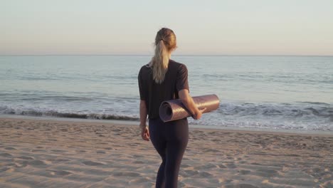 travel girl walking towards calming ocean on beach with a yoga mat