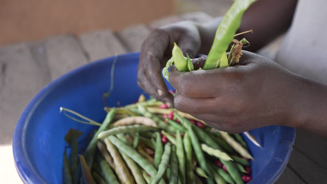 primer plano de una mujer negra africana local pelando, extrayendo y cocinando frijoles rojos
