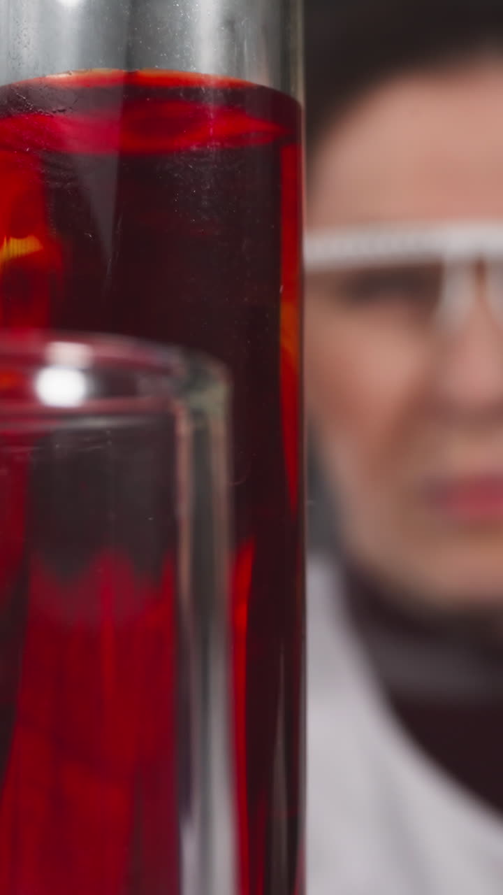 Drops of red liquid fall down into test tube under lab assistant control in laboratory slow motion. Probe lens shot of medical science closeup