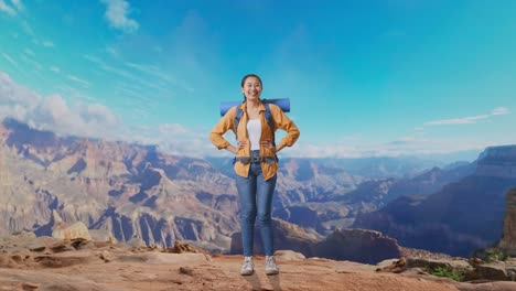 full body of asian female hiker with mountaineering backpack smiling and posing arms akimbo while traveling at the top of mountain