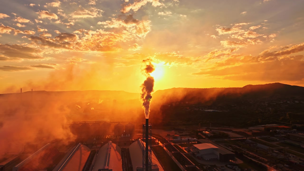 Tramonto su zona industriale con fumo che sale dalle ciminiere delle fabbriche e nuvole colorate nel cielo