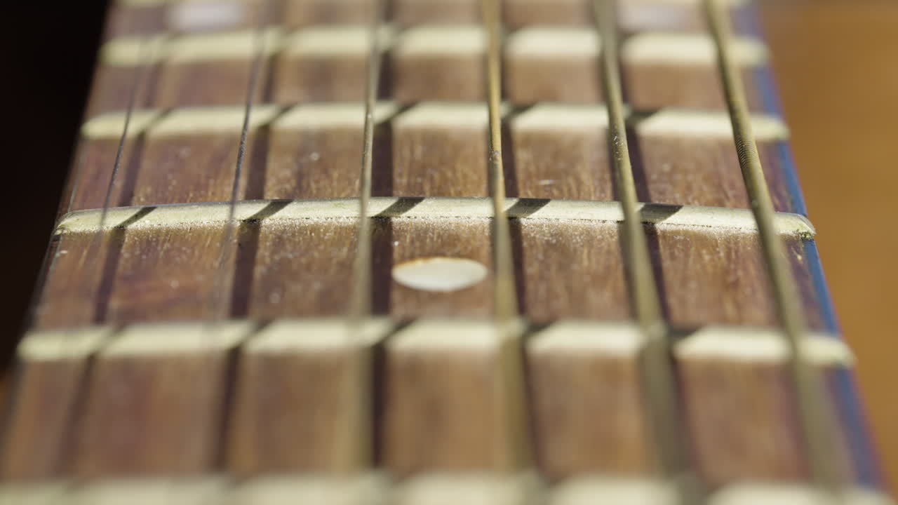 Primissimo piano con carrellata lungo le corde e i tasti del manico di una chitarra acustica. Ideale per documentari musicali e montaggi artistici.