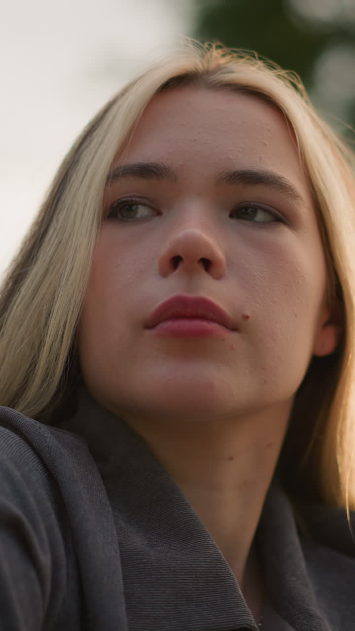dama de camisa gris profundamente en pensamiento con la luz del sol creando un brillo cálido y ambiental a su alrededor, luz suave reflejándose en su rostro, con un fondo natural borroso
